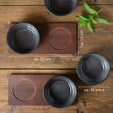 Vier anthrazitfarbene Miso-Schalen auf einem Holztisch, von oben betrachtet, mit zwei rechteckigen Untersetzern und einem Minzzweig.