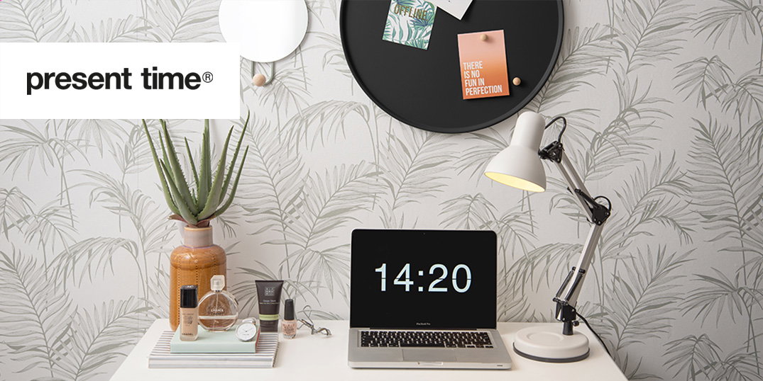 Ein stilvoller Arbeitsbereich mit einem Laptop, der die Uhrzeit anzeigt, dekorativen Pflanzen, einer Schreibtischlampe und Notizen auf einer schwarzen Wandtafel.