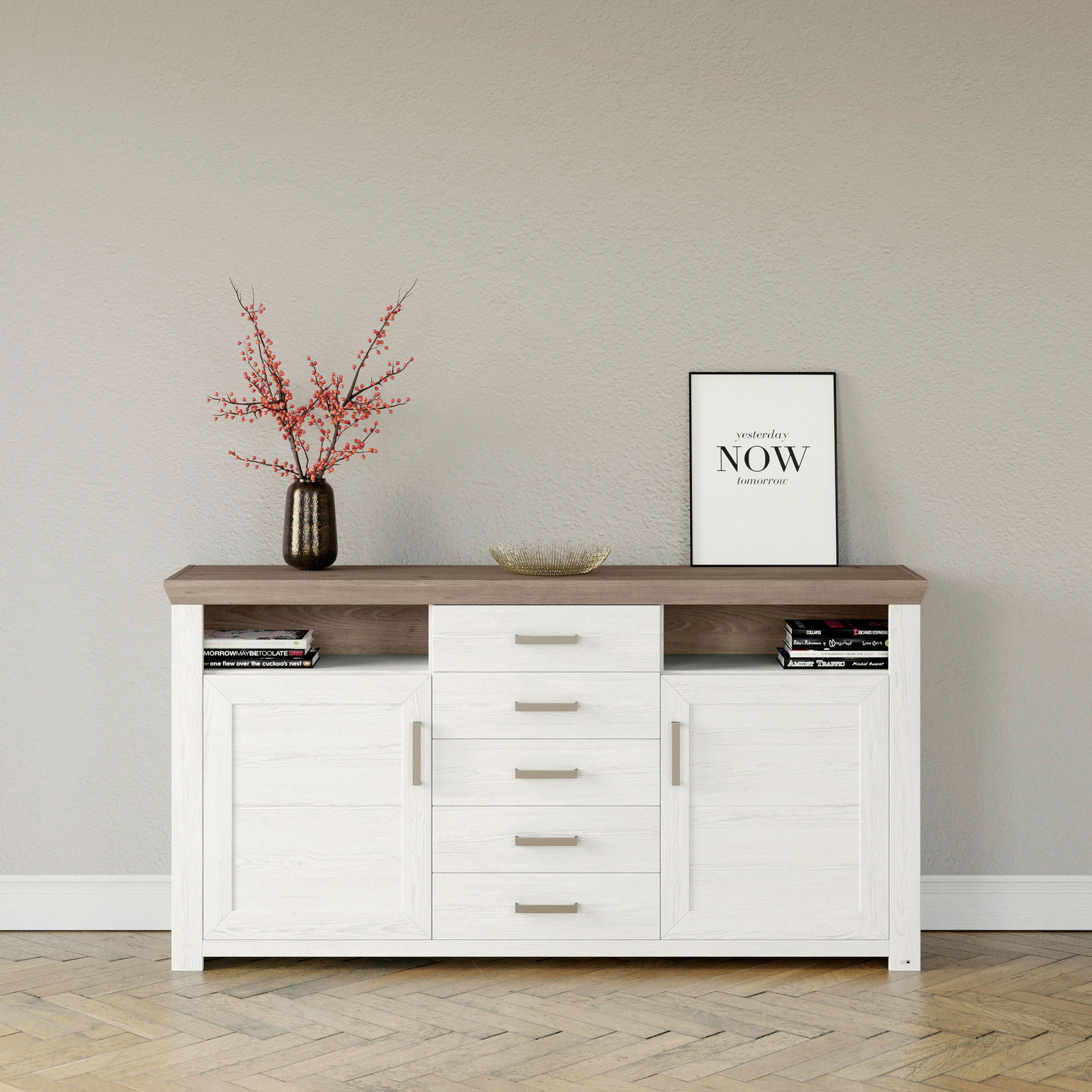 Weißes Sideboard mit brauner Oberseite, fünf Schubladen und zwei Türen, dekoriert mit einer Vase mit roten Zweigen und einem gerahmten Zitat, Frontalansicht.