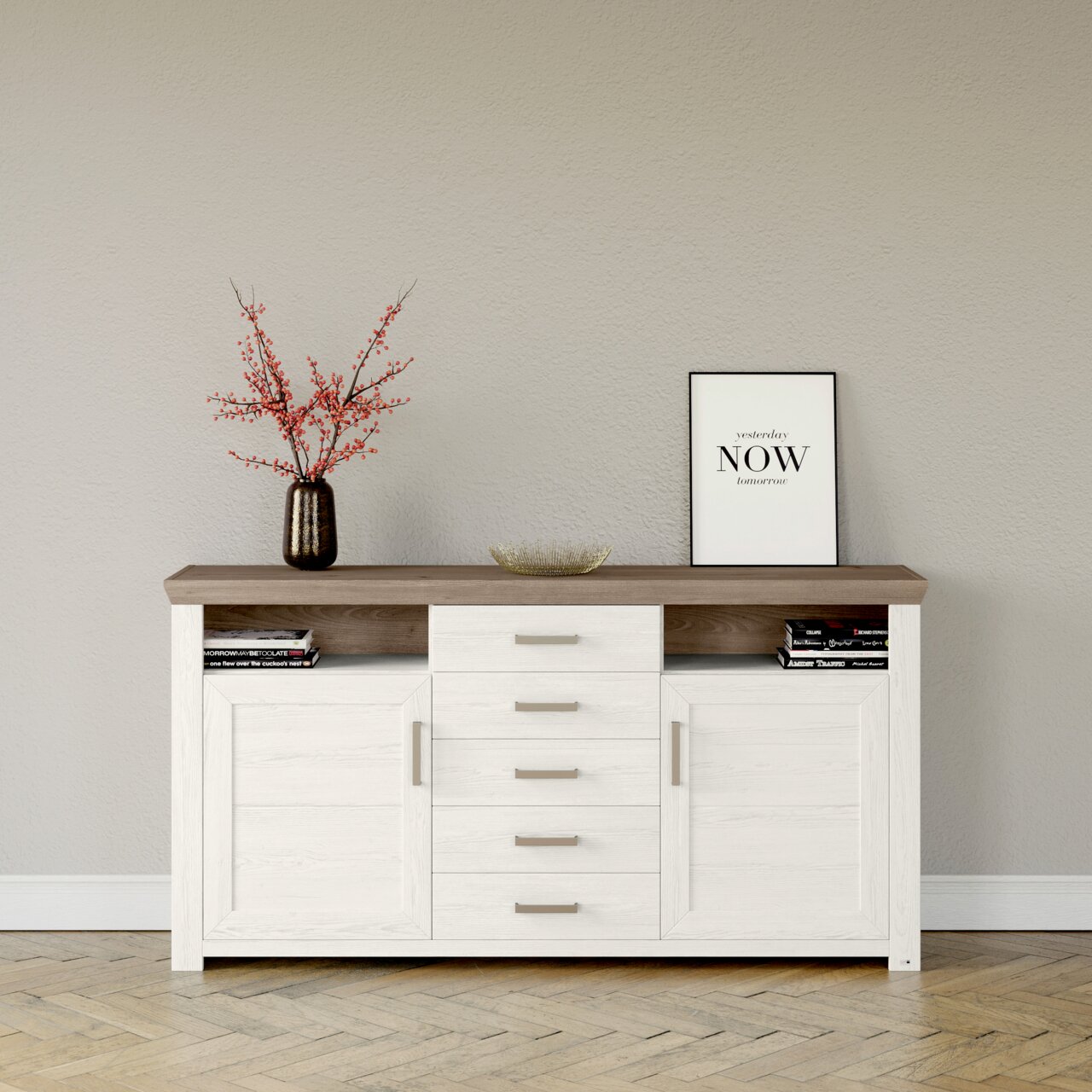 Weißes Sideboard mit brauner Oberseite, fünf Schubladen und zwei Türen, dekoriert mit einer Vase mit roten Zweigen und einem gerahmten Zitat, Frontalansicht.