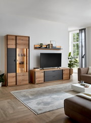 Modernes Wohnzimmer-Setup mit Wohnwand aus Holzdekor und anthrazitfarbenen Fronten, bestehend aus Vitrine mit Beleuchtung, TV-Lowboard und Wandboard, frontal in leichter Schrägansicht von rechts aufgenommen.