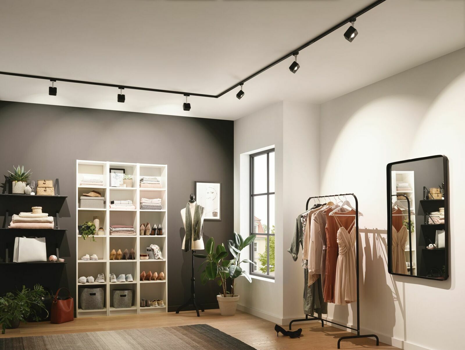 Innenraum eines modernen Ankleidezimmers mit Schienenbeleuchtung an der Decke, Regalen voller Kleidung und Accessoires, einem Kleiderständer mit eleganten Kleidern und einem großen Spiegel an der Wand. Perspektive von der Seite.