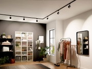 Innenraum eines modernen Ankleidezimmers mit Schienenbeleuchtung an der Decke, Regalen voller Kleidung und Accessoires, einem Kleiderständer mit eleganten Kleidern und einem großen Spiegel an der Wand. Perspektive von der Seite.