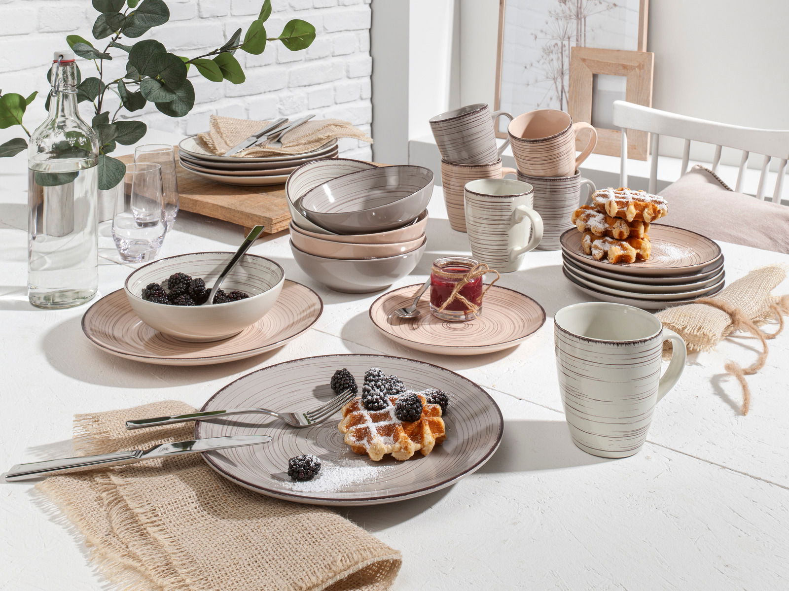 Kombiservice 24-tlg. in natürlichem Design, bestehend aus Tellern, Schalen und Tassen in sanften Erdtönen, auf einem gedeckten Tisch mit Waffeln und Beeren, aus seitlicher Perspektive fotografiert.