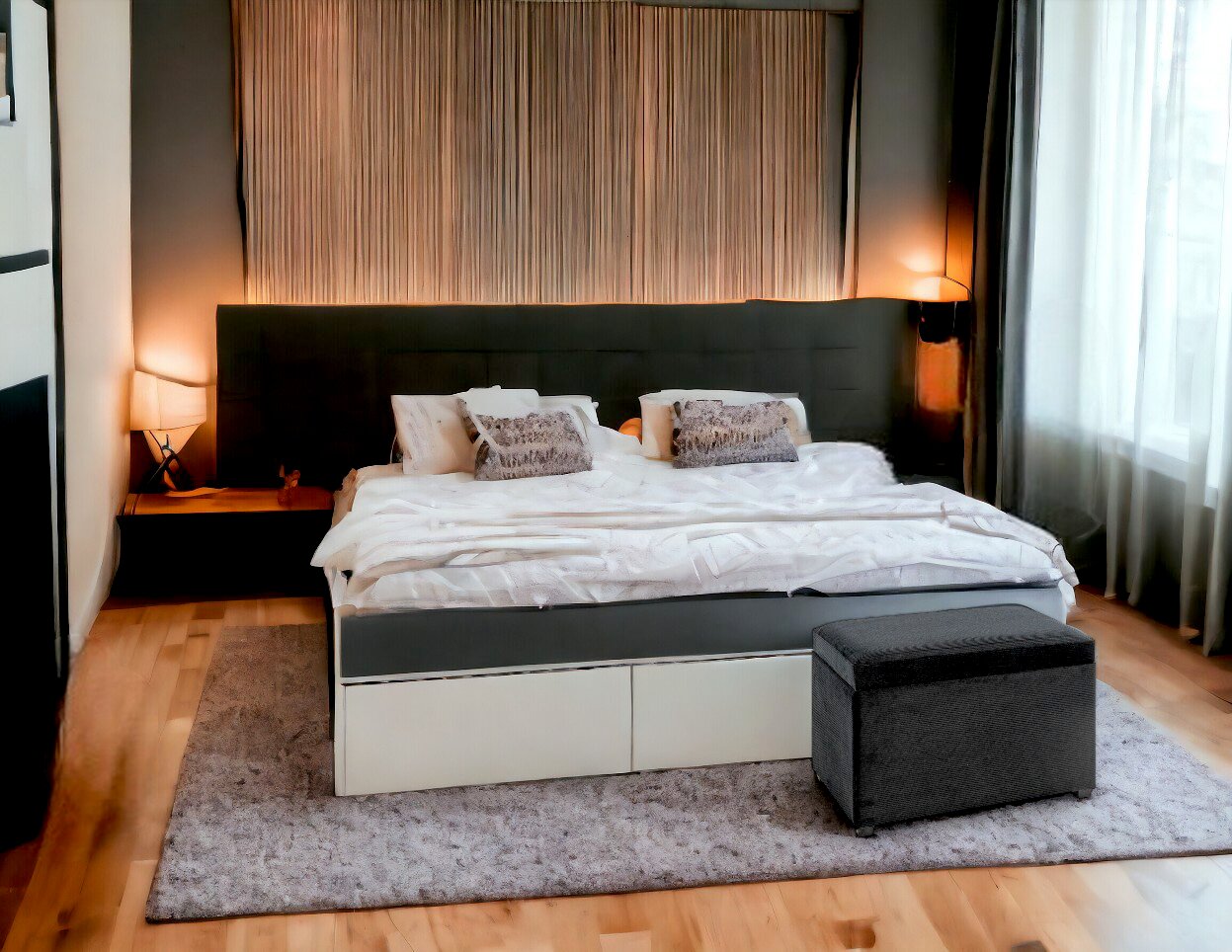 Zurbrüggen Sitztruhe DROPSHIPPING Modernes Doppelbett mit dunkel gepolstertem Kopfteil, weißer Bettwäsche und grauem Hocker am Fußende in einem Schlafzimmer mit Nachttischen und warmen Lampenlicht, Frontansicht leicht erhöht.