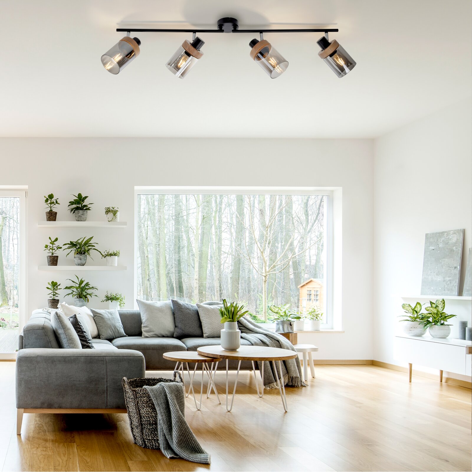 Moderne Decken-Spotleuchte mit vier verstellbaren Strahlern, schwarzer Schiene, Glaszylindern und Holzdetails, montiert an der Decke; Perspektive: leicht nach oben aus dem Wohnzimmer (Untersicht).