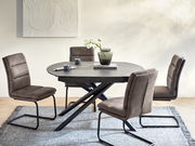 Runder Esstisch mit schwarzer Platte und gekreuzten Beinen, umgeben von vier gepolsterten Stühlen in einem modernen Esszimmer, seitliche Perspektive.