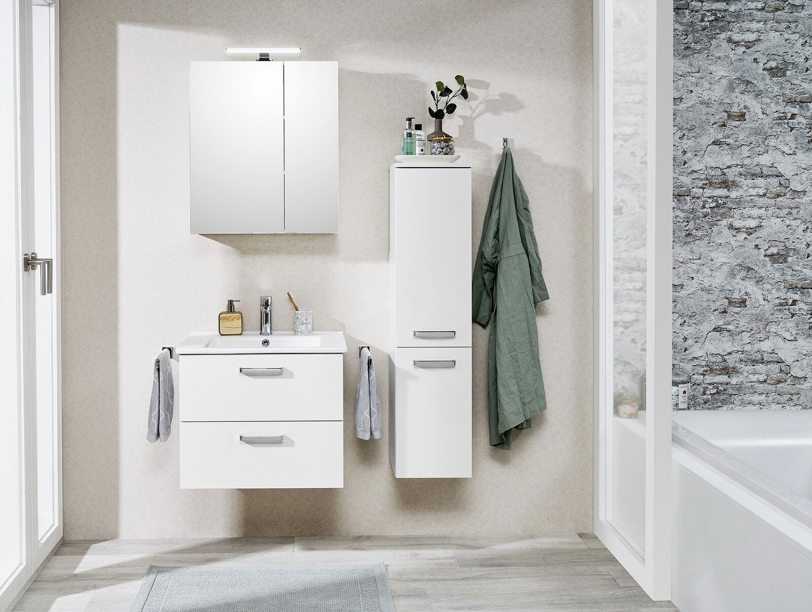 XORA Waschtischlösung TIVOLI Moderne Waschtischlösung in einem Badezimmer, frontal fotografiert. Enthält einen weißen Waschtisch mit zwei Schubladen, einen Spiegel und einen hohen Schrank. Dekoriert mit Handtüchern und Pflanzen.