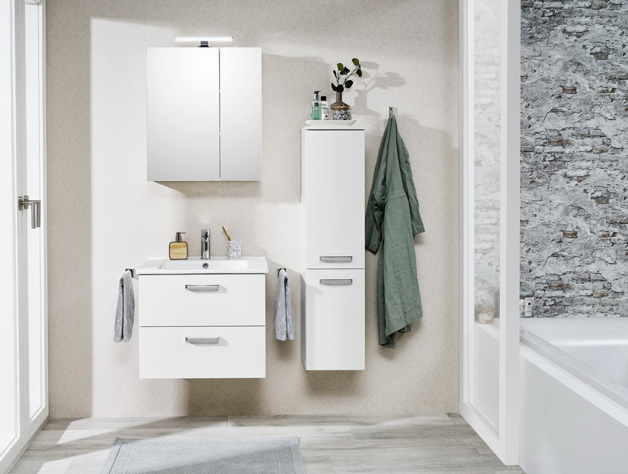 Moderne Waschtischlösung in einem Badezimmer, frontal fotografiert. Enthält einen weißen Waschtisch mit zwei Schubladen, einen Spiegel und einen hohen Schrank. Dekoriert mit Handtüchern und Pflanzen.