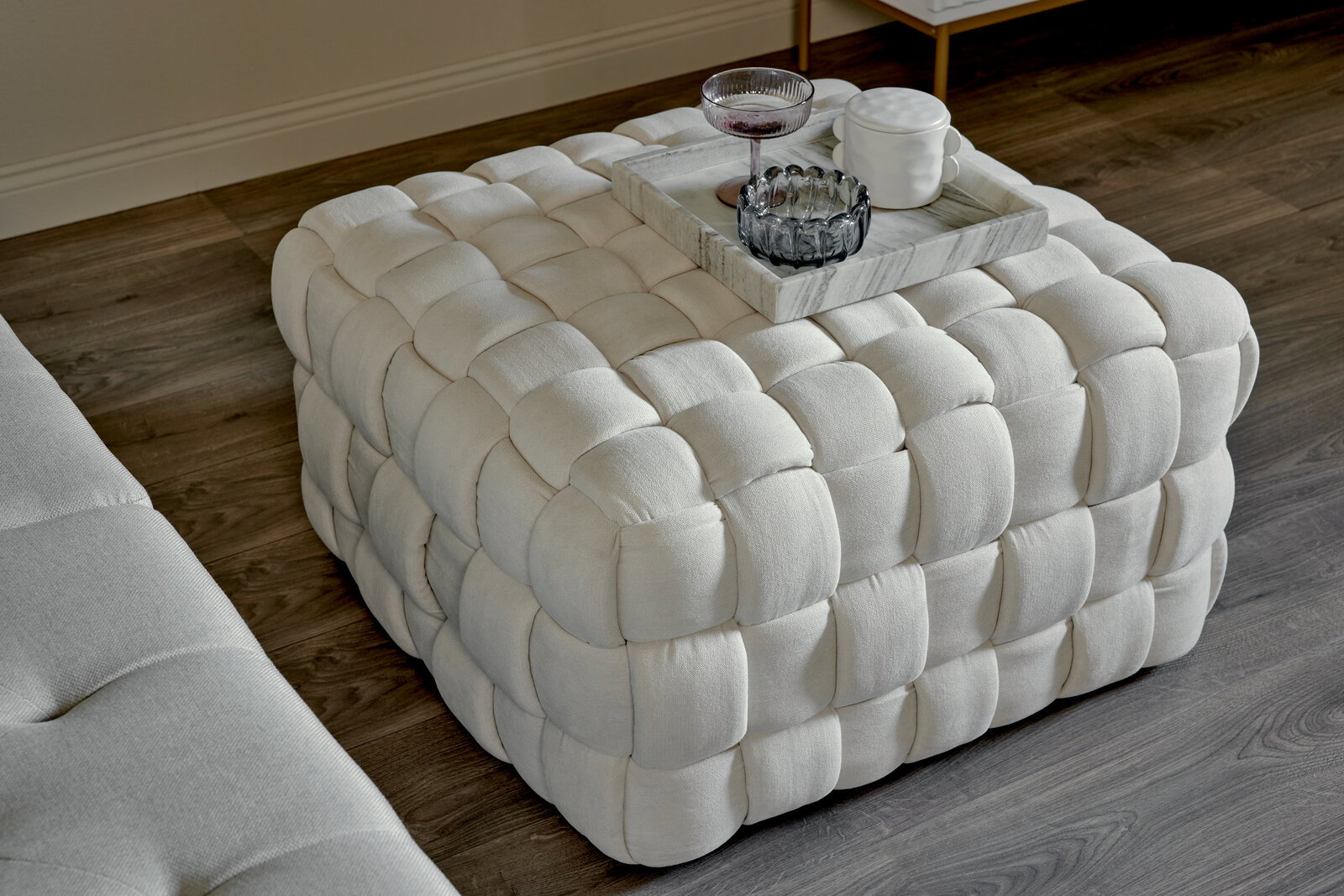 Weißer, gepolsterter Hocker mit quadratischem Muster, von oben betrachtet, mit einem Tablett und Gläsern darauf.