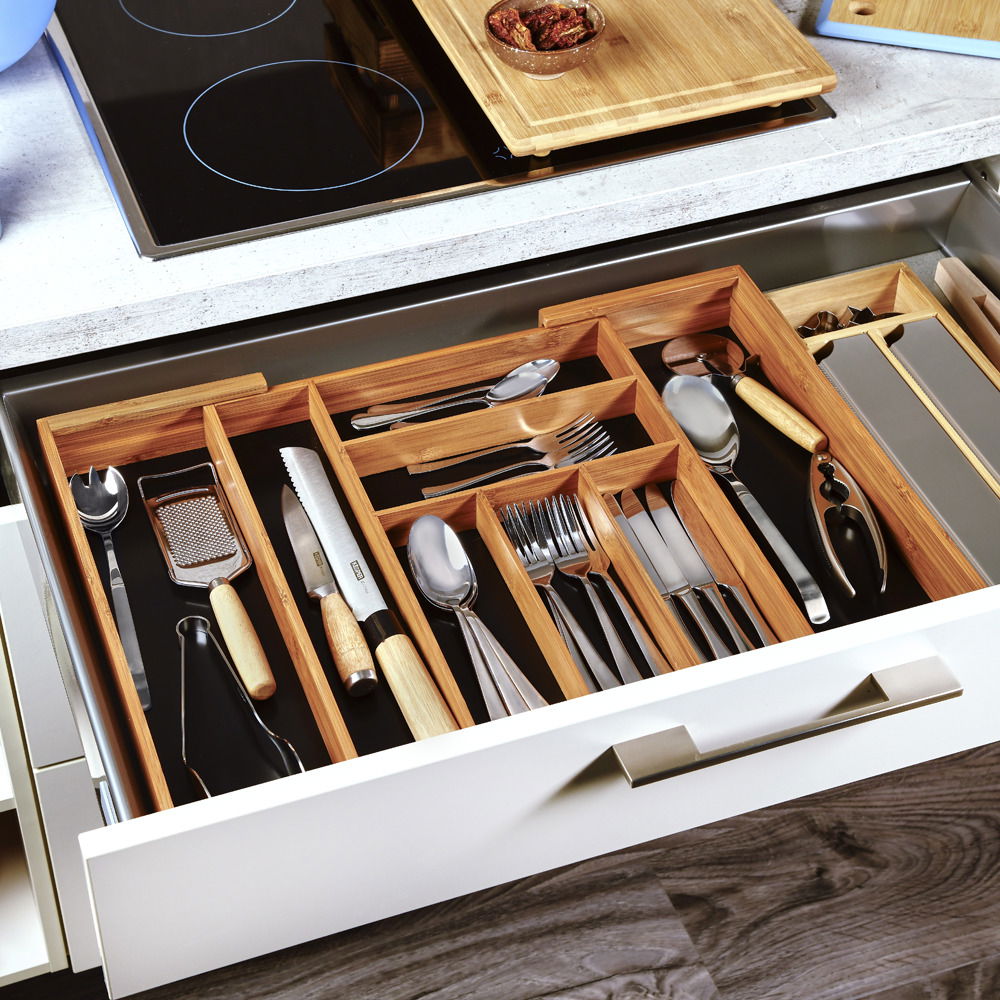 Variabler Besteckkasten aus Holz in einer geöffneten Küchenschublade, gefüllt mit verschiedenen Besteck- und Küchenutensilien, aus der Vogelperspektive.