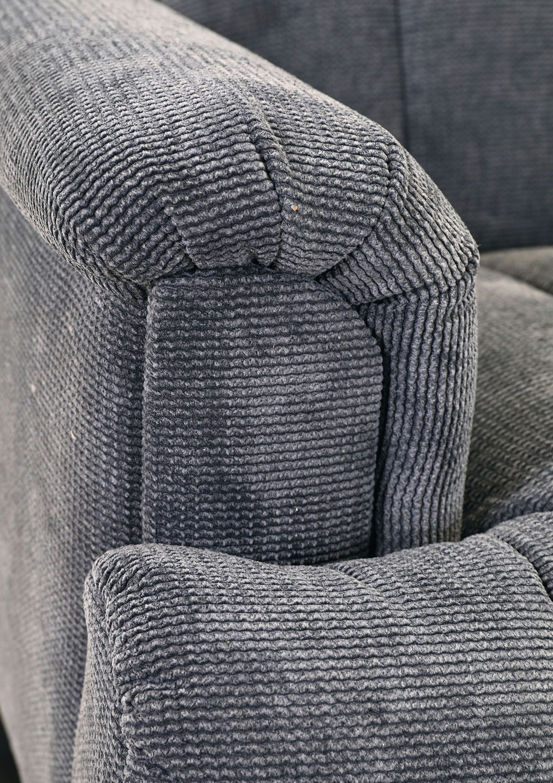 Nahaufnahme einer grauen, strukturierten Polsterung eines Sofas, Perspektive von der Armlehne.