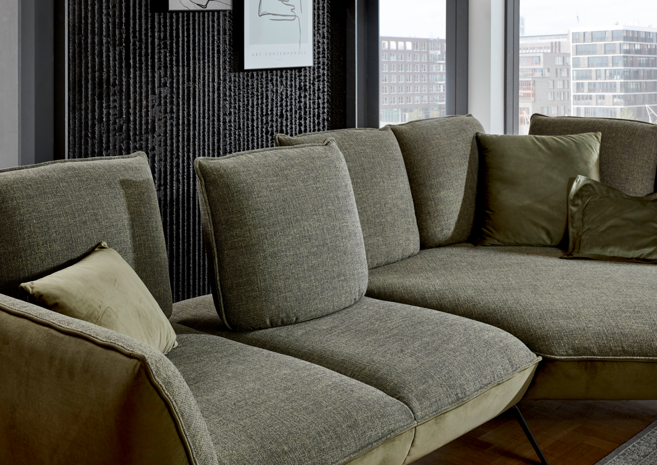 Moderano Longchairkombination ALPHA Moderano Longchairkombination ALPHA in einer modernen Wohnumgebung, seitliche Perspektive auf das grüne Sofa mit mehreren Kissen.