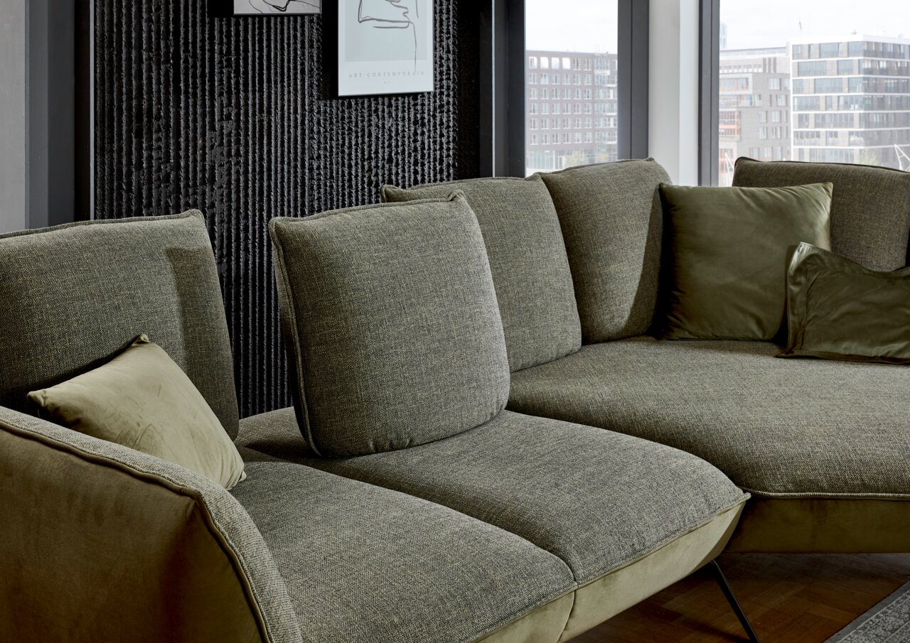 Moderano Longchairkombination ALPHA in einer modernen Wohnumgebung, seitliche Perspektive auf das grüne Sofa mit mehreren Kissen.