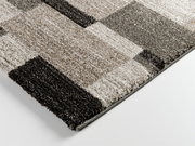 Nahaufnahme eines Hochflorteppichs Castle Beppo in rechteckigem Design mit verschiedenen Grautönen und geometrischem Muster, perspektivisch von der Seite aufgenommen.