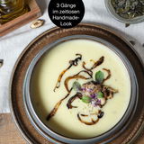 Vogelperspektive auf einen Teller mit cremiger Suppe, garniert mit gebratenen Zwiebeln und frischen Kräutern, serviert auf einem rustikalen, braunen Tafelservice.