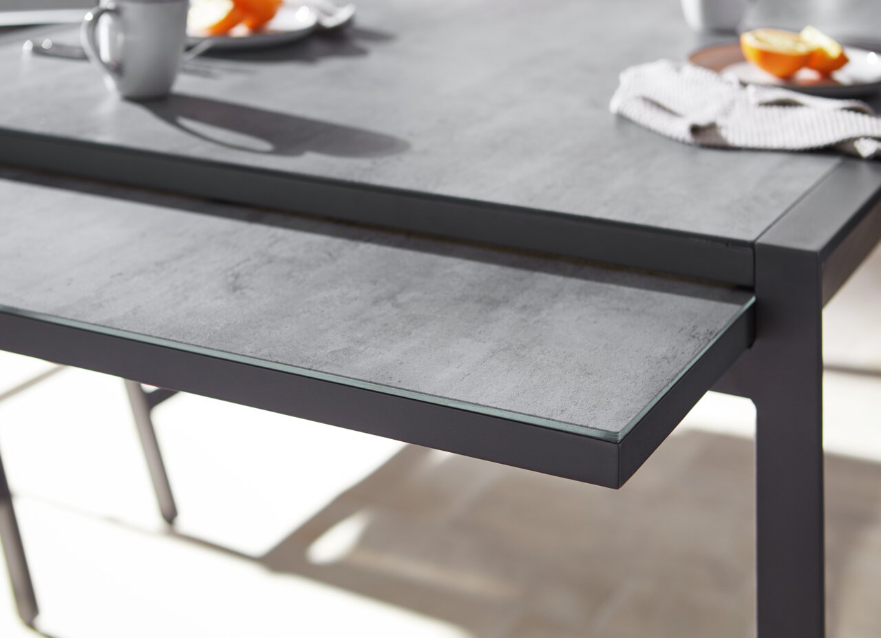 Nahaufnahme eines modernen Gartentisches mit grauer Steinoptik-Oberfläche und schwarzem Metallrahmen, seitliche Perspektive