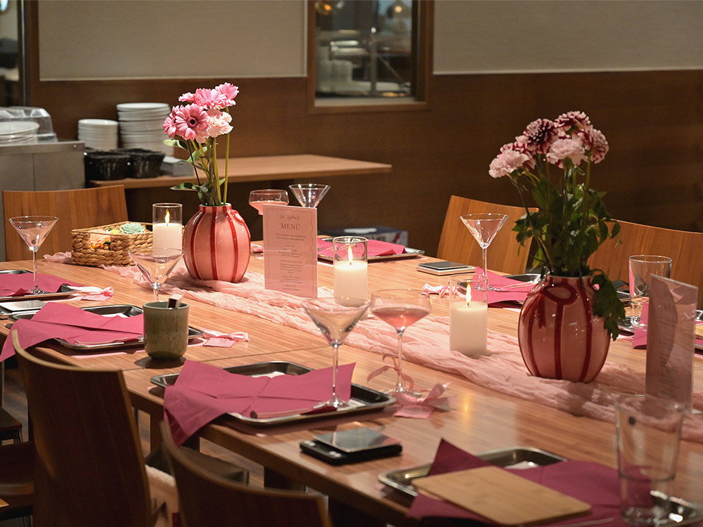 Feestelijk gedekte tafel met roze servetten, bloemen, kaarsen en glazen tijdens een creatieve Get Together.