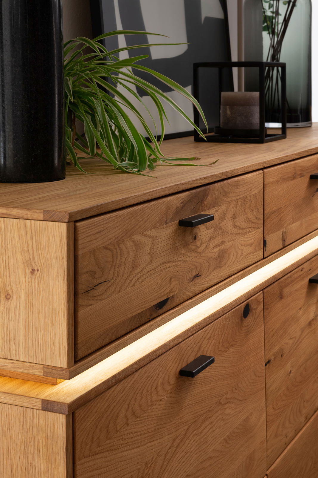 Nahaufnahme eines modernen Sideboards aus Holz mit Schubladen und integrierter Beleuchtung, dekoriert mit Pflanzen und Accessoires, seitliche Perspektive.