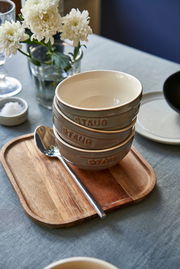 Drei graue Schüsseln mit der Aufschrift 'STAUB' gestapelt auf einem Holztablett, seitliche Perspektive.