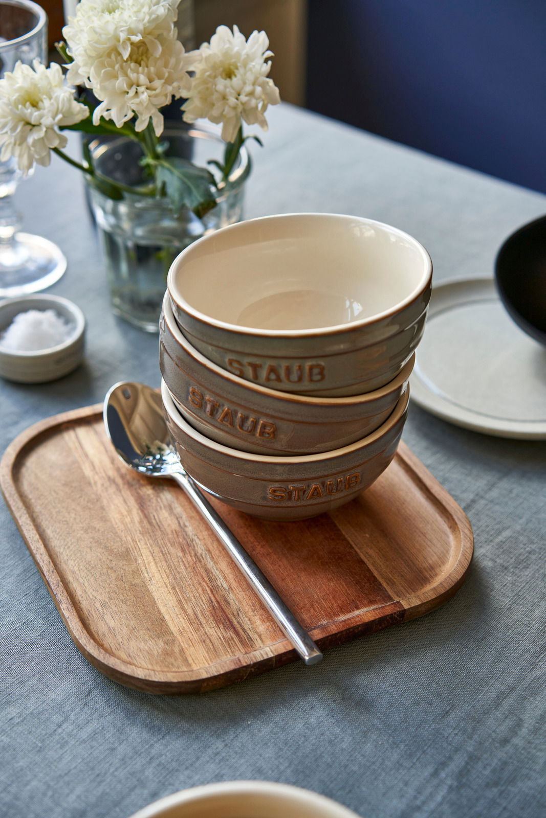 Drei graue Schüsseln mit der Aufschrift 'STAUB' gestapelt auf einem Holztablett, seitliche Perspektive.