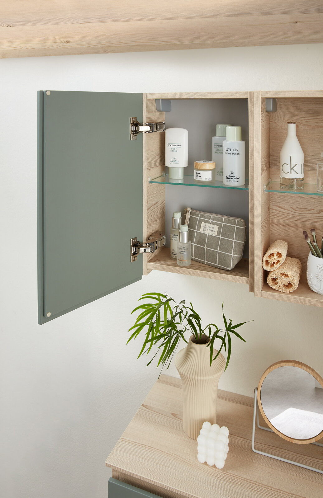 Geöffneter Hängeschrank mit grüner Tür, gefüllt mit Pflegeprodukten und Accessoires, aus der Seitenperspektive fotografiert.