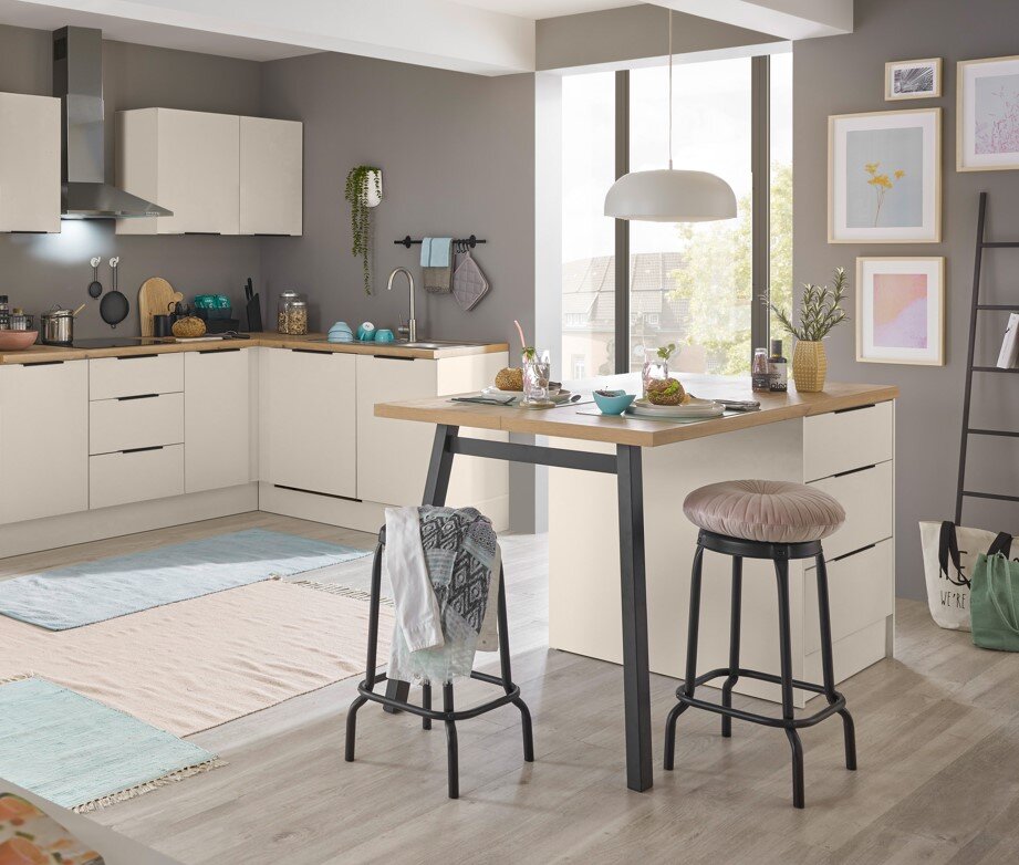 Yourkitchen Eckunterschrank MULTAN Moderne L-förmige Küche in Beige mit Holzarbeitsplatte und Kücheninsel/Esstisch, zwei Barhockern und Pendelleuchte, aufgenommen in leichter Schrägansicht von vorn im hellen Raum