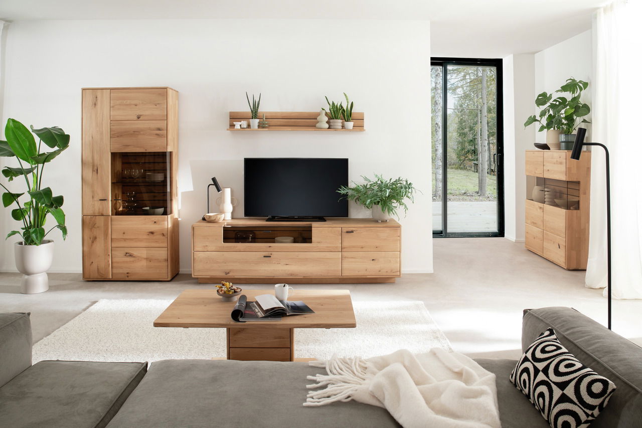 Wohnzimmeransicht mit der Linea Natura Wandkombination GEORGIA in hellem Holz, bestehend aus einem TV-Schrank, einem hohen Schrank und einem Wandregal, dekoriert mit Pflanzen und modernen Accessoires.