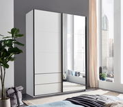 Moderner, zweiflügeliger Schwebetürenschrank mit Spiegel, in einem hellen Raum mit großen Fenstern, aus der Perspektive von schräg vorne fotografiert.