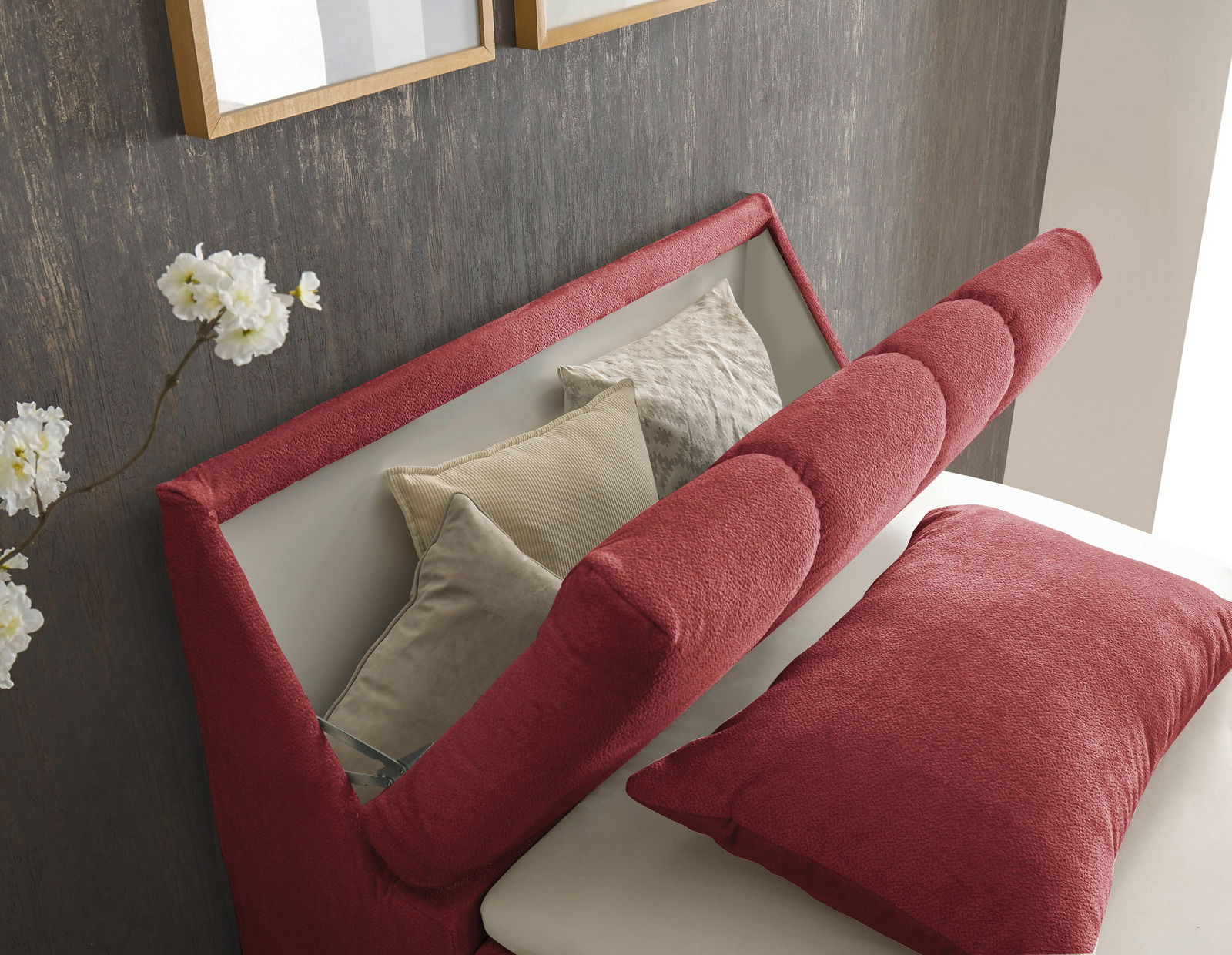 Nahaufnahme eines Boxspringbetts mit rotem Kopfteil und Kissen, seitliche Perspektive
