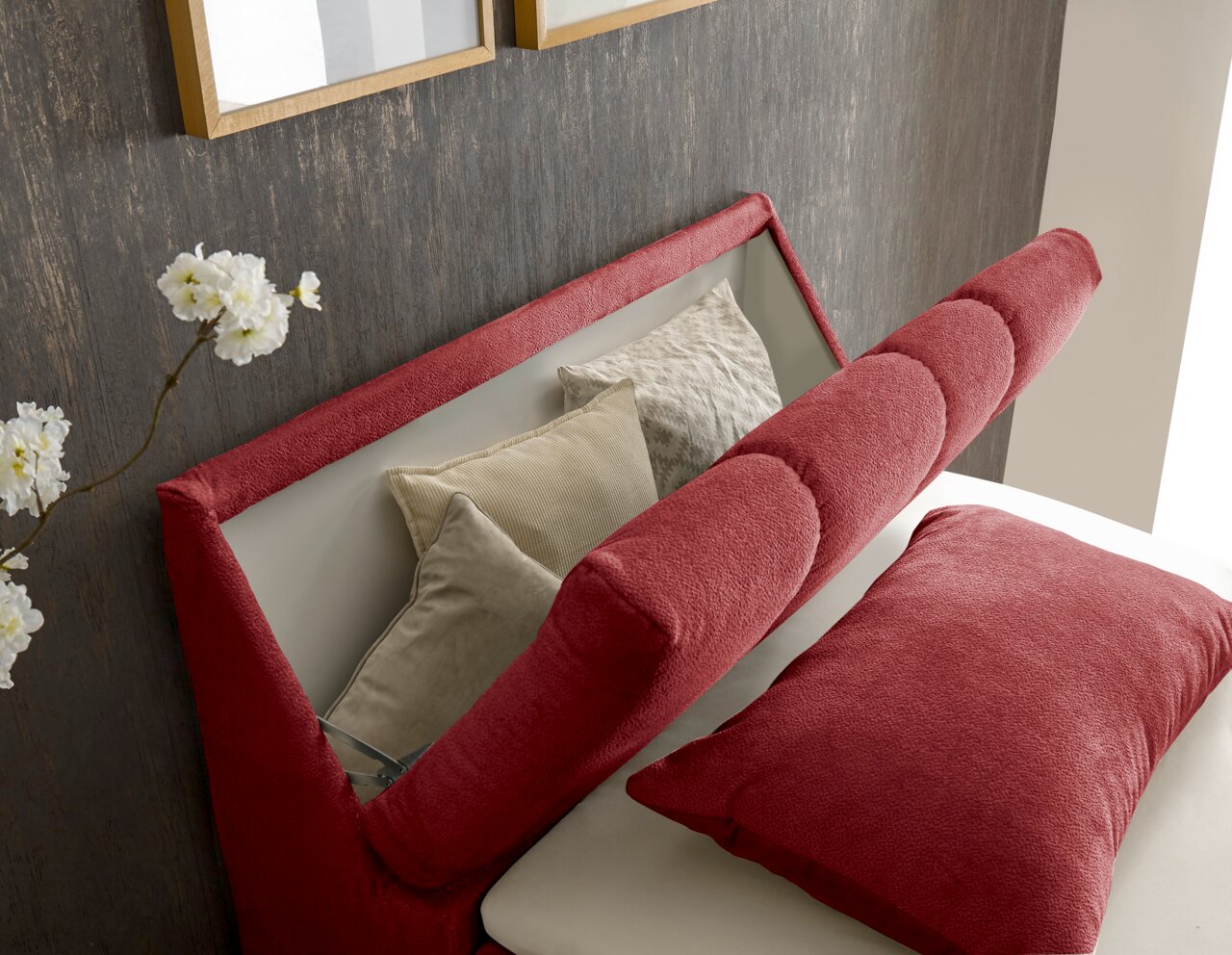 Nahaufnahme eines Boxspringbetts mit rotem Kopfteil und Kissen, seitliche Perspektive