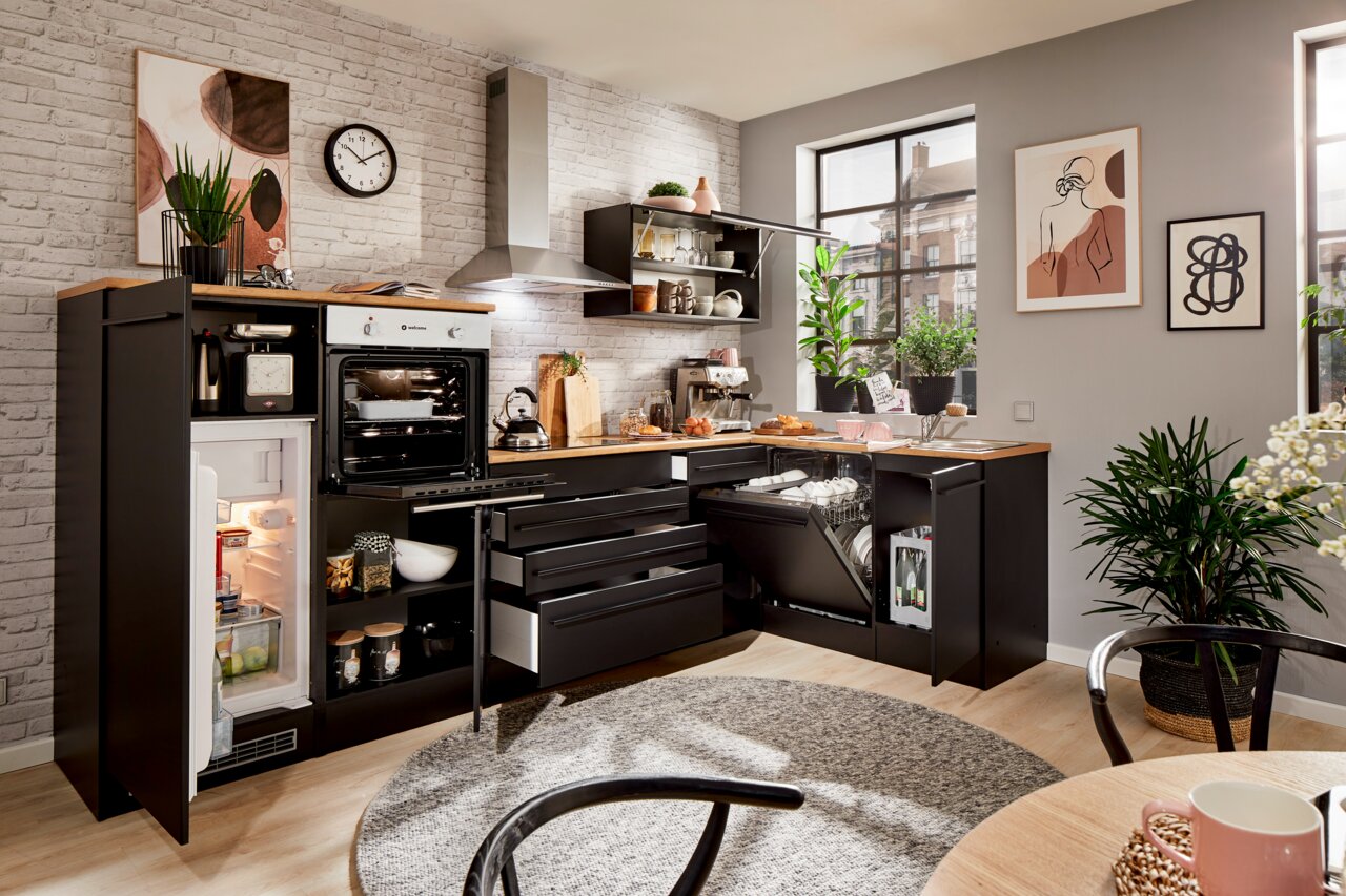 Moderne Küche mit Eckunterschrank, Kühlschrank, Backofen und Geschirrspüler in schwarzem Design, fotografiert aus einer leicht erhöhten Perspektive.