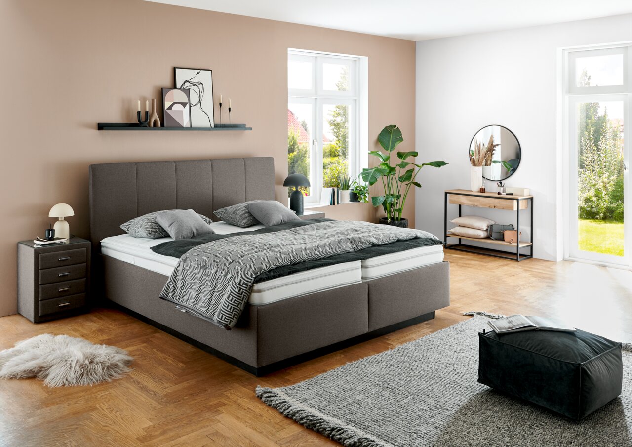 Modern gestoffeerd bed in een stijlvol ingerichte slaapkamer, zijaanzicht met nachtkastje, planten en decoratie.