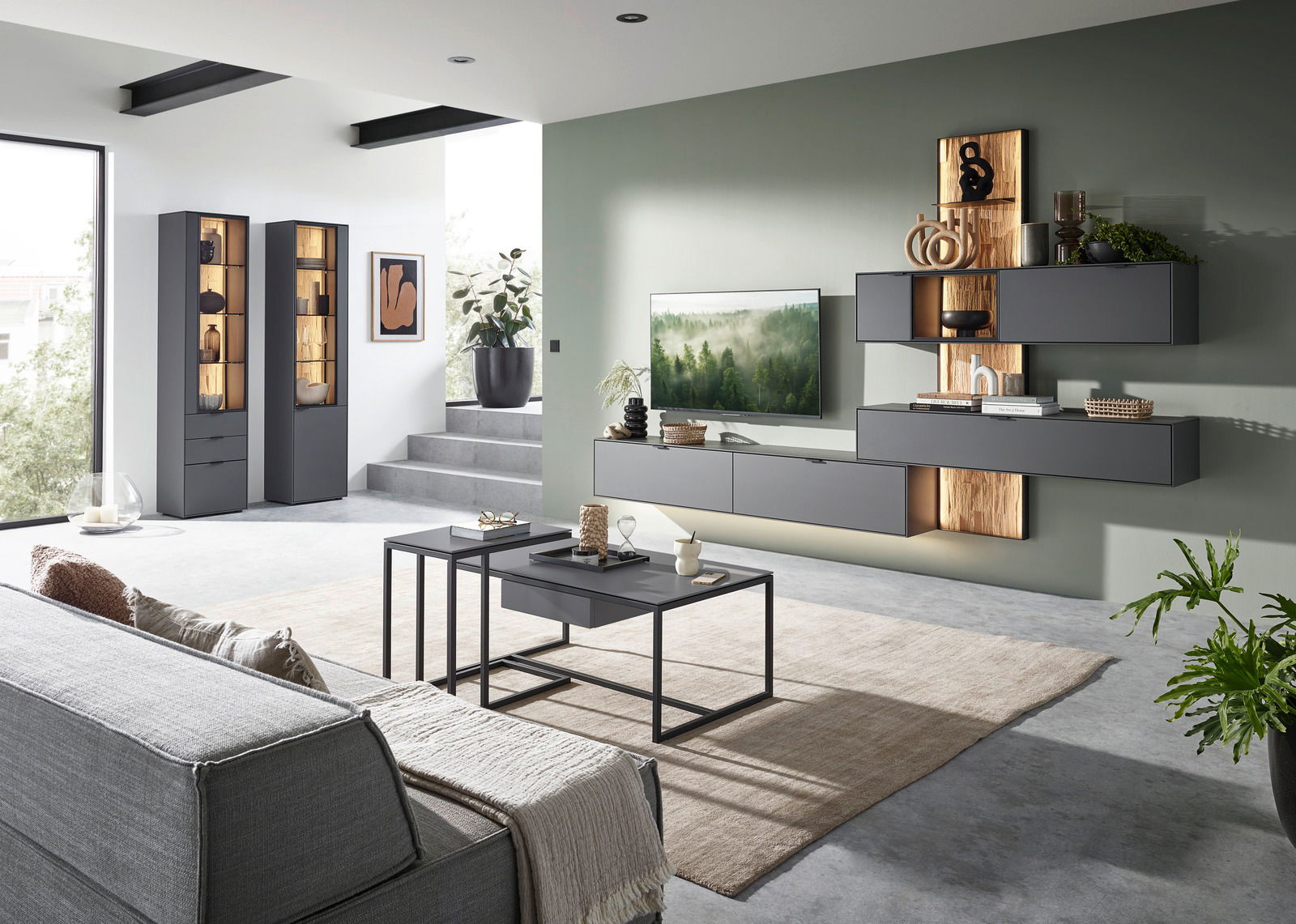 Moderne Wohnzimmerwandkombination in Grau mit Holzakzenten, bestehend aus hängenden Schränken und Regalen, mit dekorativen Elementen und einem Fernseher, aus der Perspektive des Wohnzimmers betrachtet.