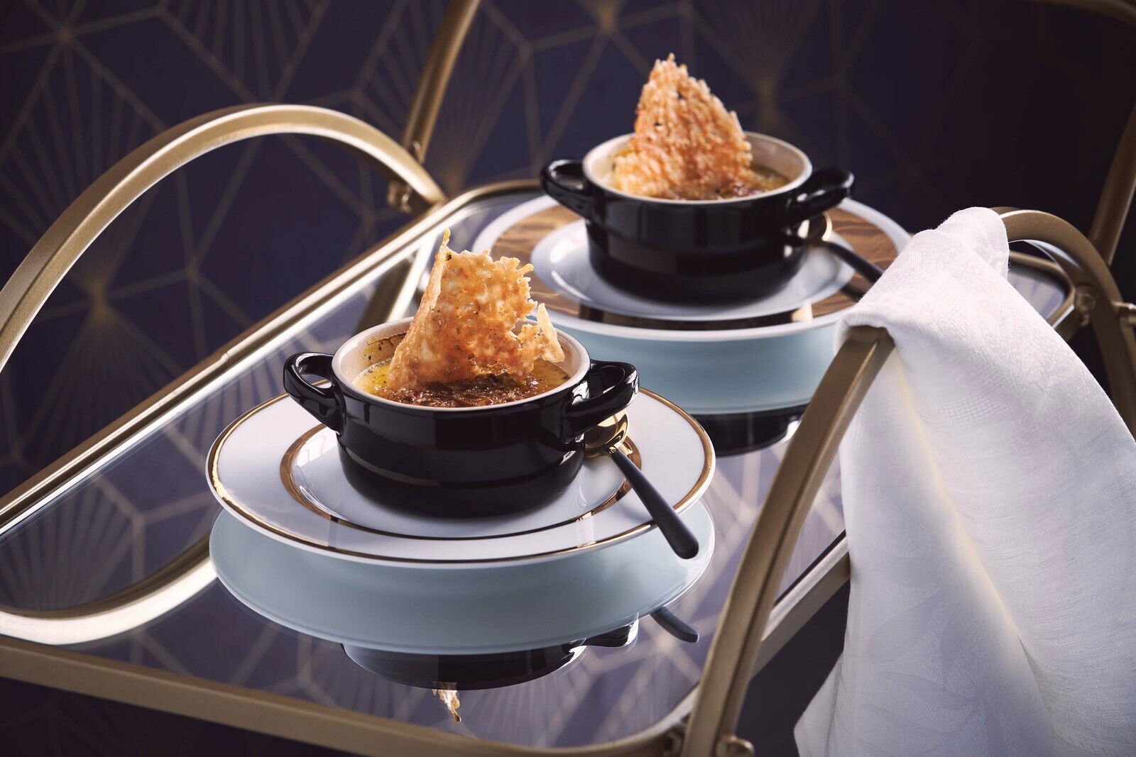 Schwarze Mini-Cocotte auf einem eleganten Tisch, gefüllt mit einer Speise und dekoriert mit einem knusprigen Topping, seitliche Perspektive