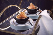 Schwarze Mini-Cocotte auf einem eleganten Tisch, gefüllt mit einer Speise und dekoriert mit einem knusprigen Topping, seitliche Perspektive