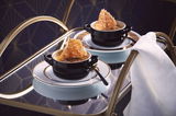 Schwarze Mini-Cocotte auf einem eleganten Tisch, gefüllt mit einer Speise und dekoriert mit einem knusprigen Topping, seitliche Perspektive