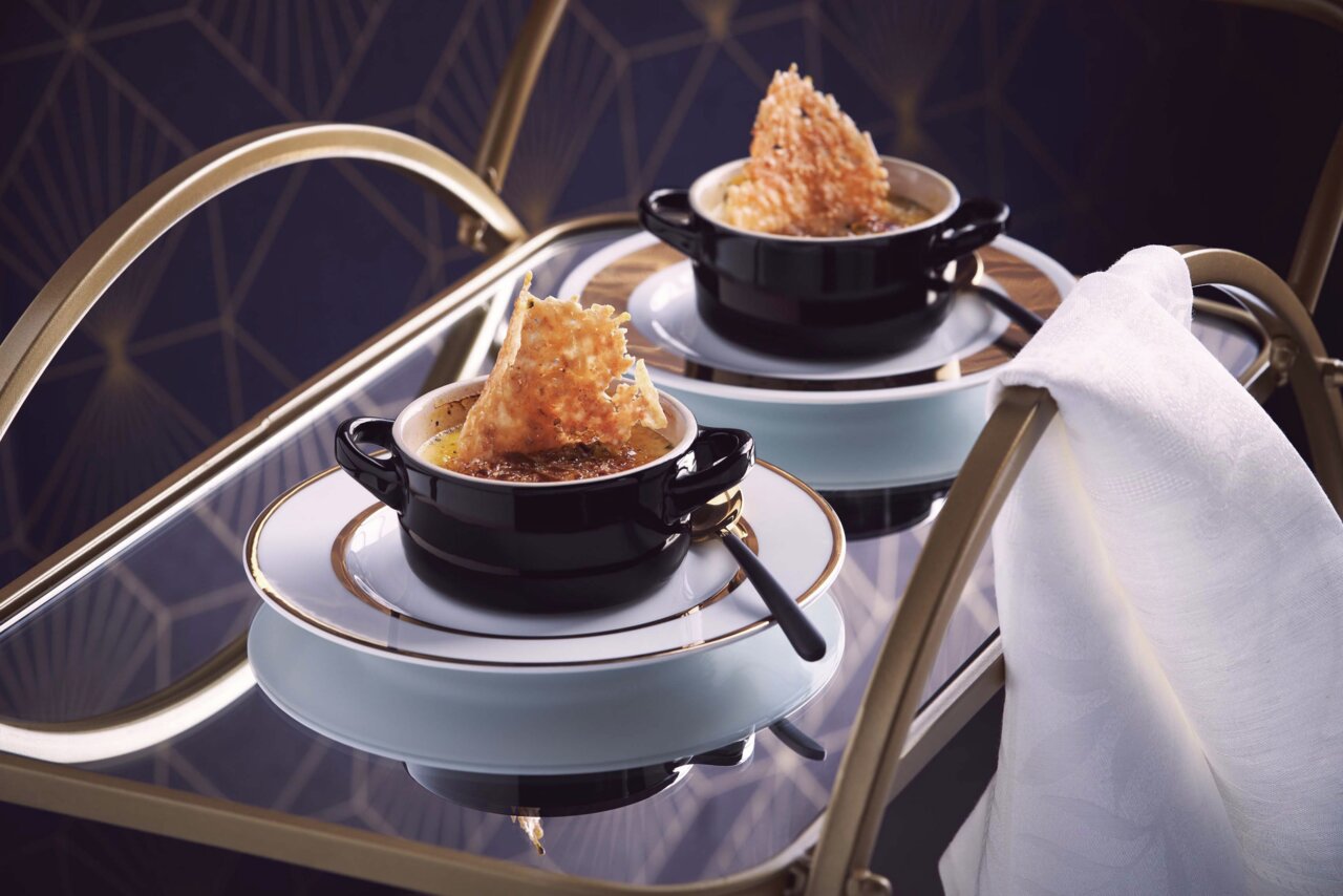 Schwarze Mini-Cocotte auf einem eleganten Tisch, gefüllt mit einer Speise und dekoriert mit einem knusprigen Topping, seitliche Perspektive