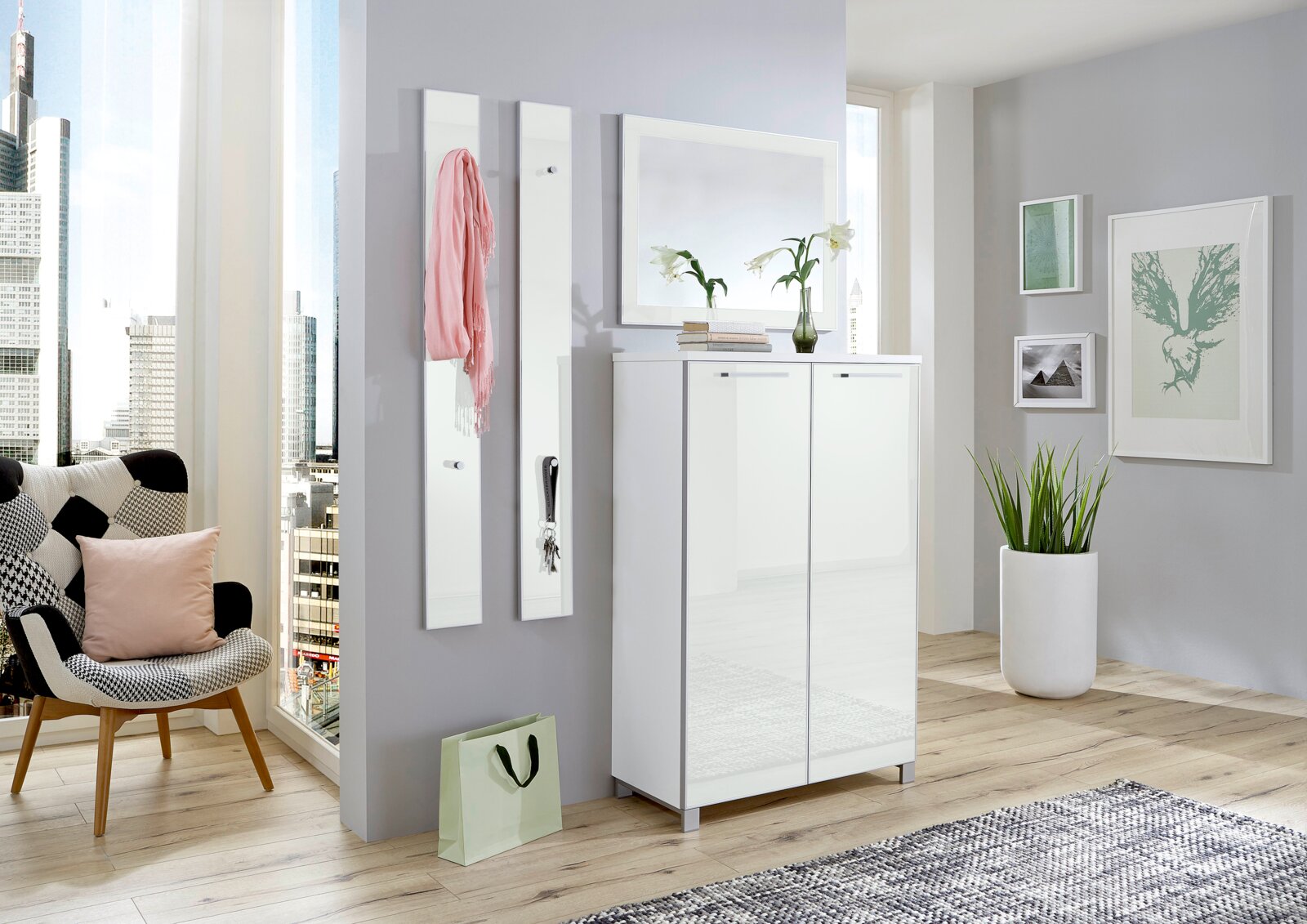 Modernes Garderoben-Set in einem hellen Raum mit Stadtblick, bestehend aus einem weißen Schrank und zwei Wandpaneelen mit Haken, aus der Frontalperspektive.