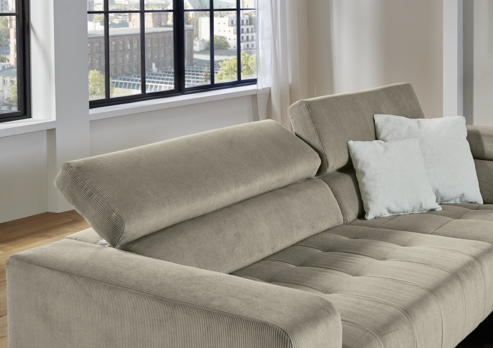 Beiges Cord-Ecksofa mit verstellbaren Rückenlehnen und hellen Kissen in modernem Wohnzimmer, schräg von vorne links fotografiert.