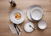 Bovenaanzicht van een stijlvol grijs-wit servies met organisch gevormde borden en kom, afgewerkt met een zwarte gestippelde rand en gepresenteerd op een houten tafel.