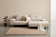 Beige Longchairkombination mit zwei Kissen und einer Decke, frontal fotografiert, auf einem Teppich neben einer Pflanze.