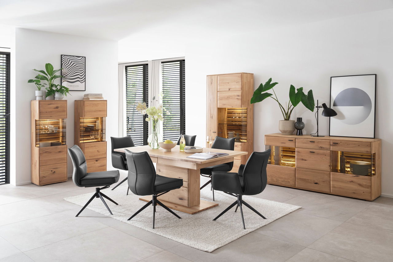 Linea Natura Highboard GEORGIA Moderne Esszimmerkombination mit Holztisch, schwarzen Stühlen und beleuchteten Vitrinen, seitliche Perspektive.