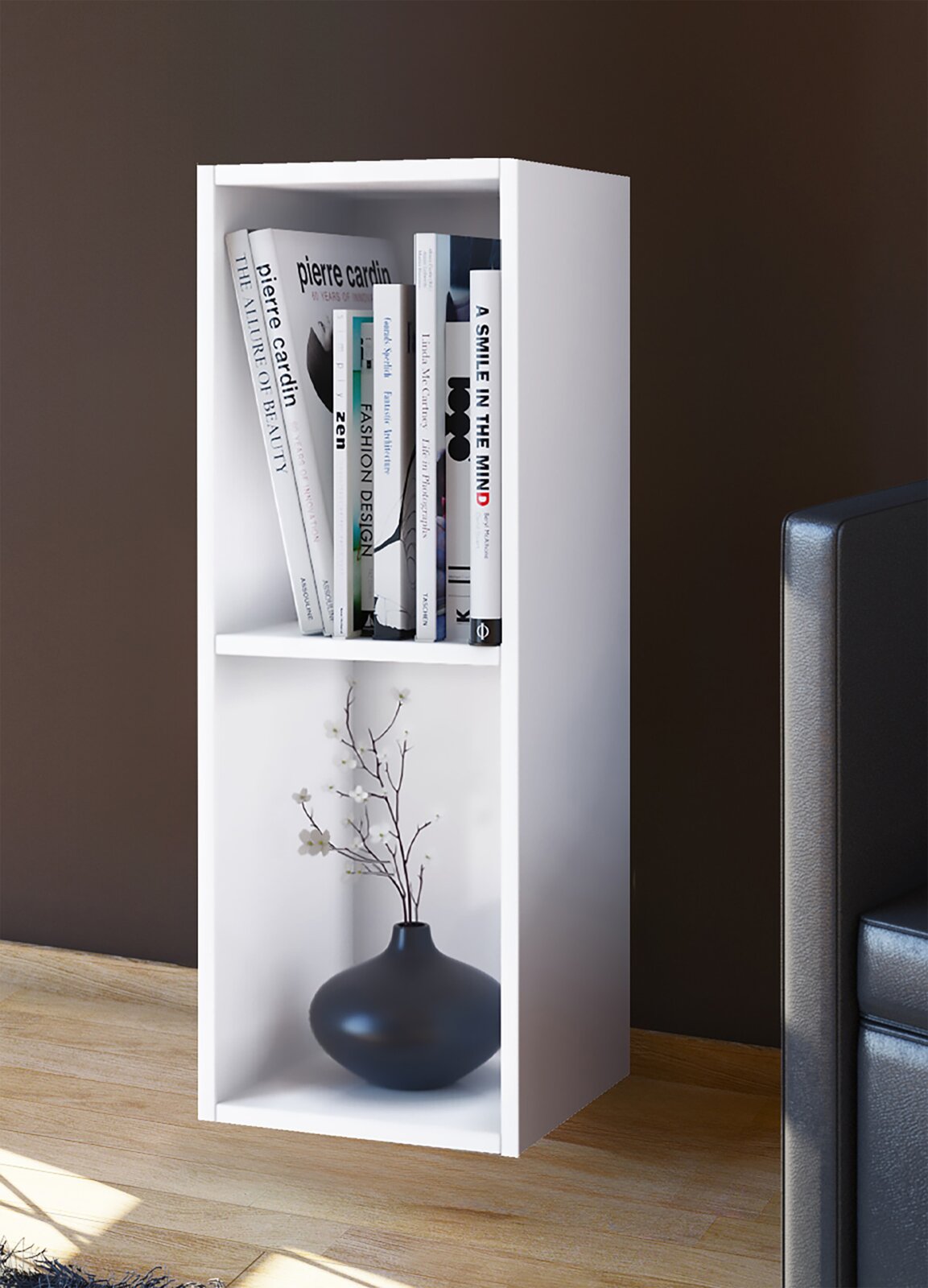 Weißes, schmales Standregal mit zwei offenen Fächern, oben mit Büchern und unten mit schwarzer Vase dekoriert, in leicht schräger Frontansicht im Wohnzimmer.