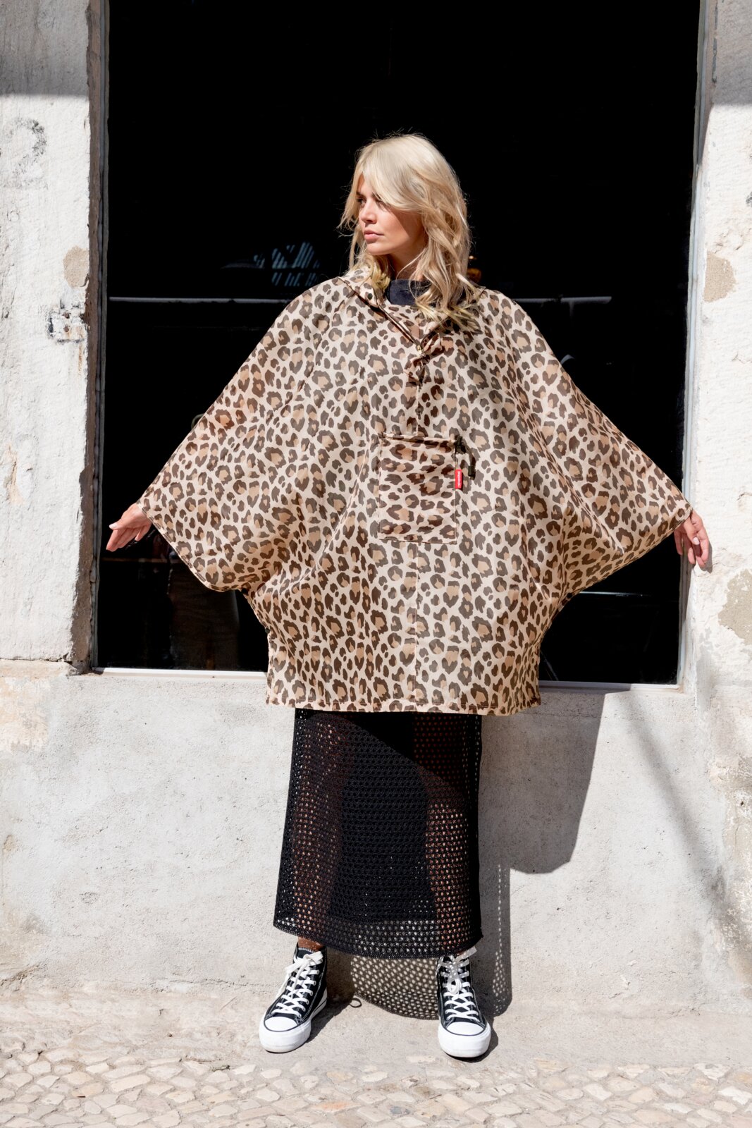 Reisenthel Mini Maxi Poncho Leo Macchiato Frau in einem Leopardenmuster-Poncho, stehend in der Sonne, Frontalansicht