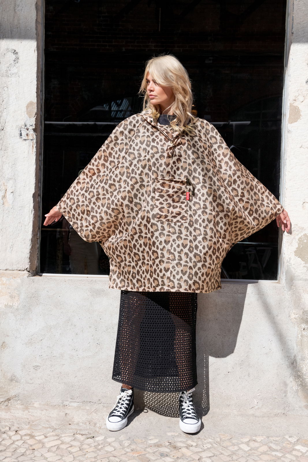 Reisenthel Mini Maxi Poncho LEO MACCHIATO Frau in einem Leopardenmuster-Poncho, stehend in der Sonne, Frontalansicht
