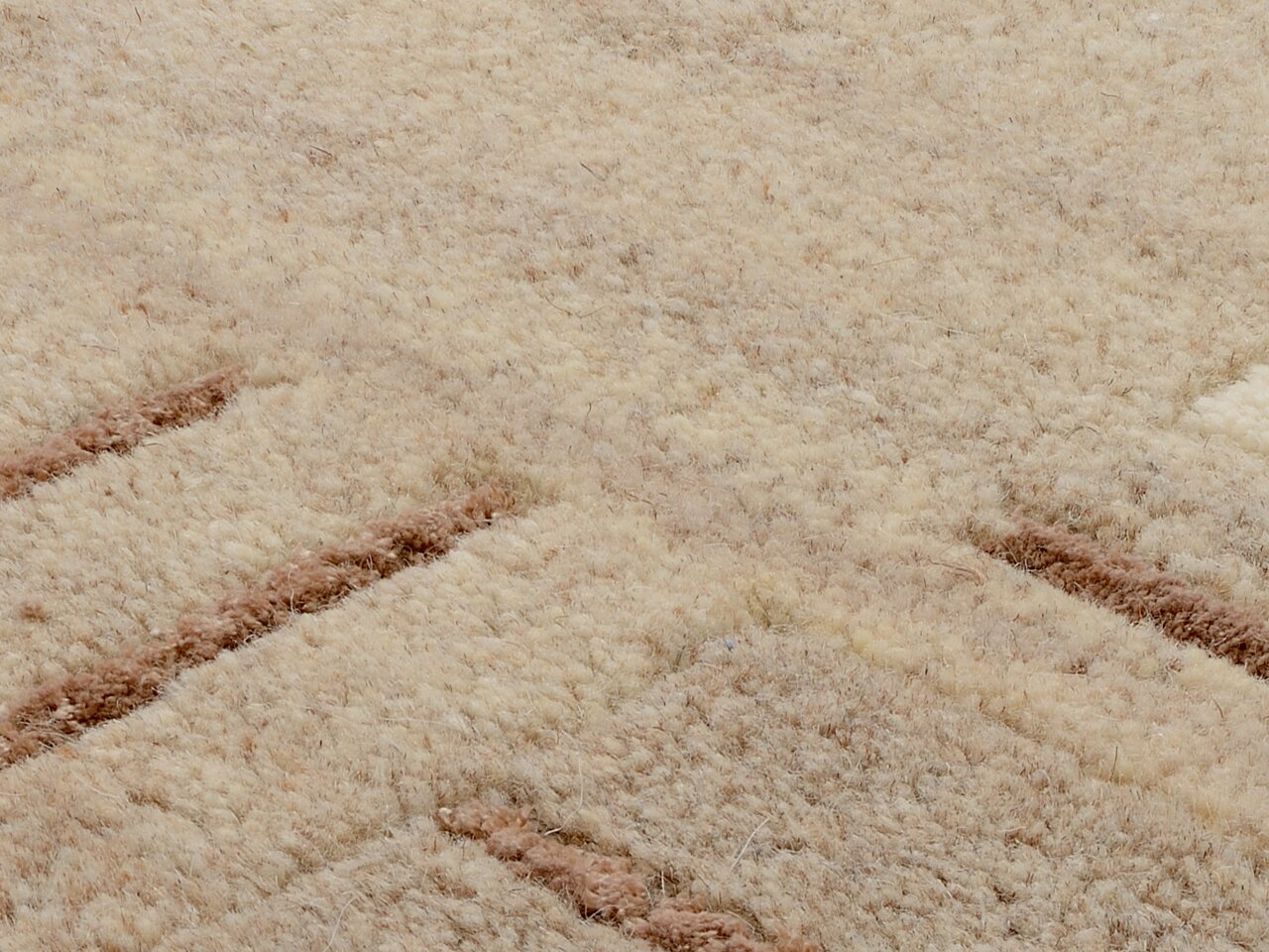 Nahaufnahme eines Wollteppichs mit beigem und braunem Muster, aus der Vogelperspektive fotografiert.