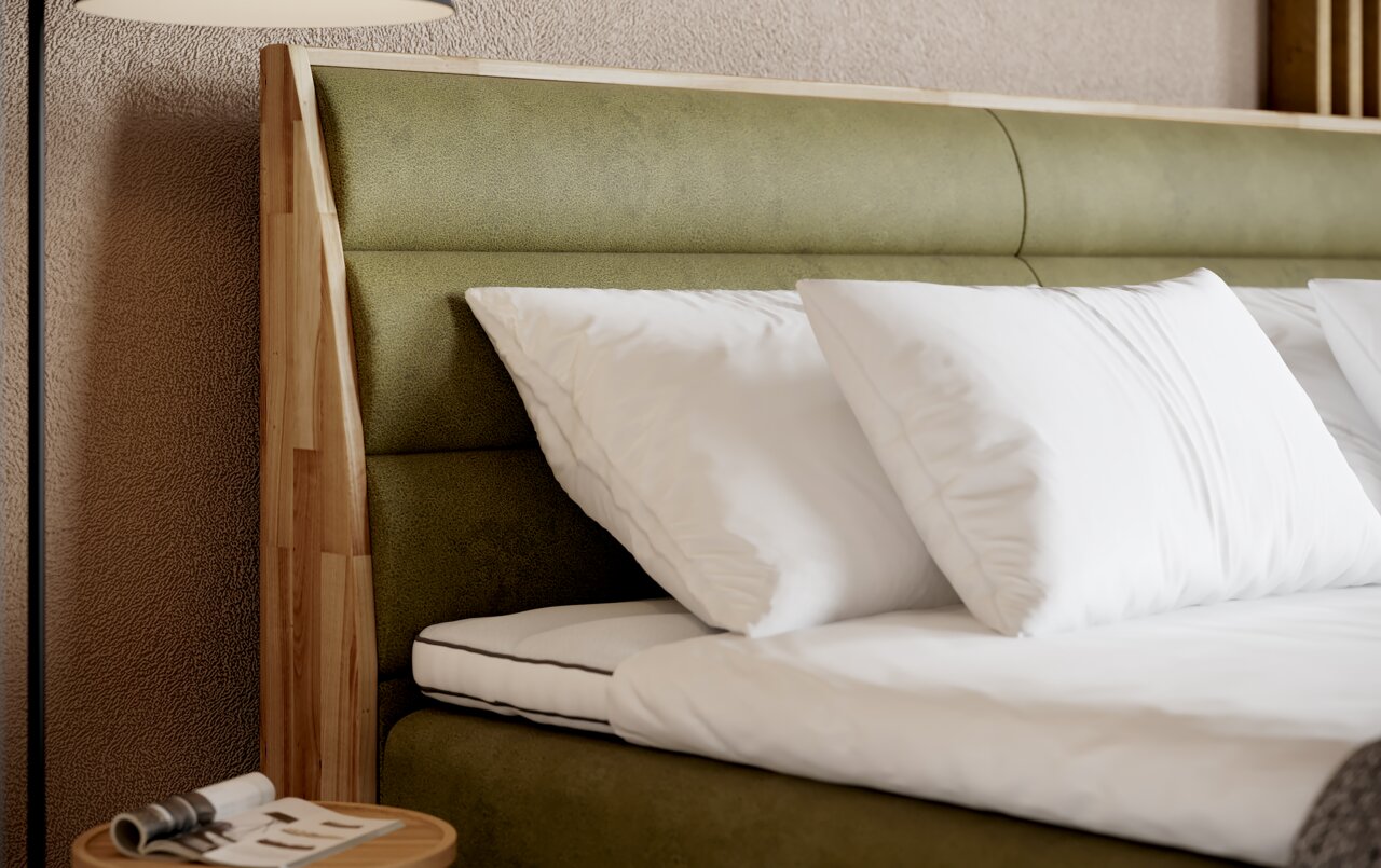 Nahaufnahme eines Boxspringbetts mit grünem Kopfteil und weißen Kissen, seitliche Perspektive