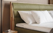 Nahaufnahme eines Boxspringbetts mit grünem Kopfteil und weißen Kissen, seitliche Perspektive