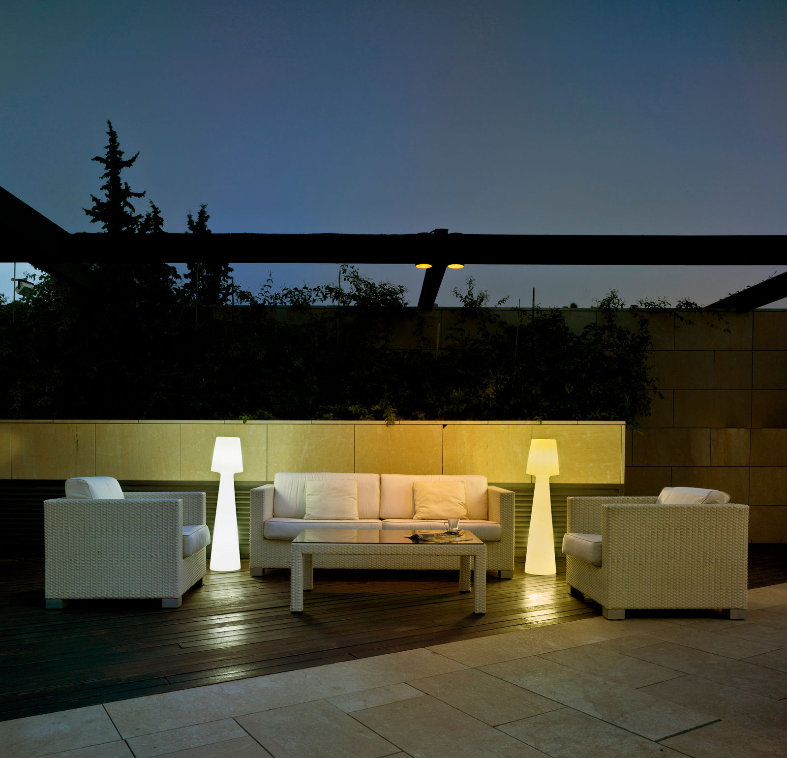 Stehleuchte LOLA 110 in einem modernen Außenbereich, umgeben von weißen Rattanmöbeln, bei Dämmerung beleuchtet.